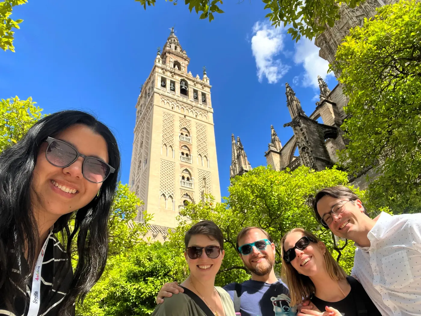 Travelers taking a group selfie beneath the Giralda tower at Seville Cathedral on a sunny day