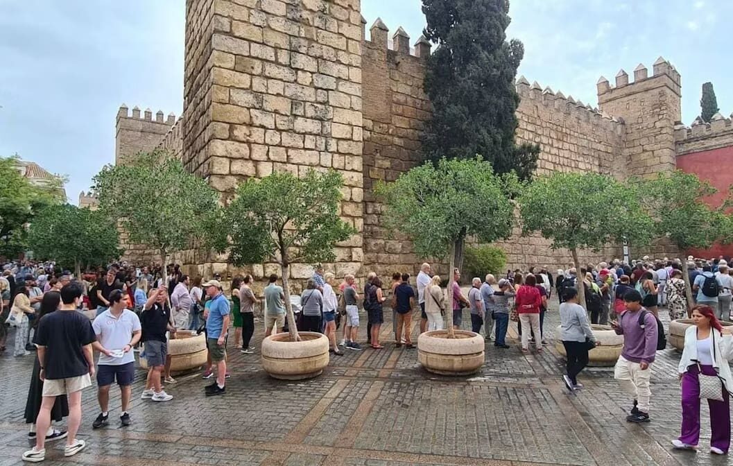 Long line of tourists waiting outside the Royal Alcázar walls, a common sight with mass tourism in Seville