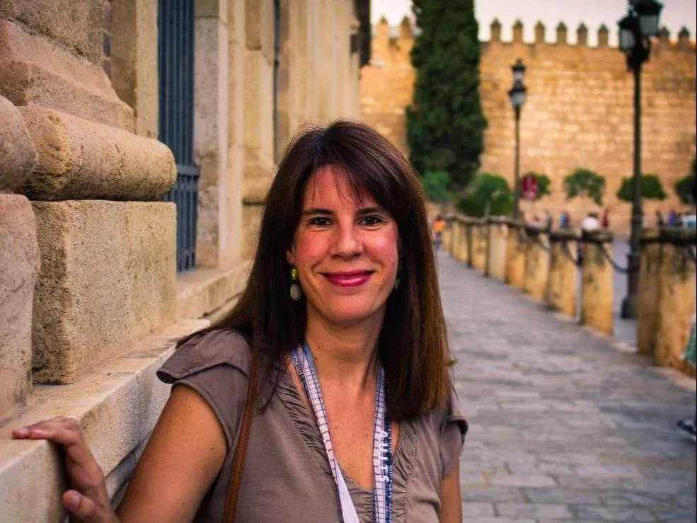 Smiling Altai Turismo guide wearing a lanyard beside historic stone walls in Seville