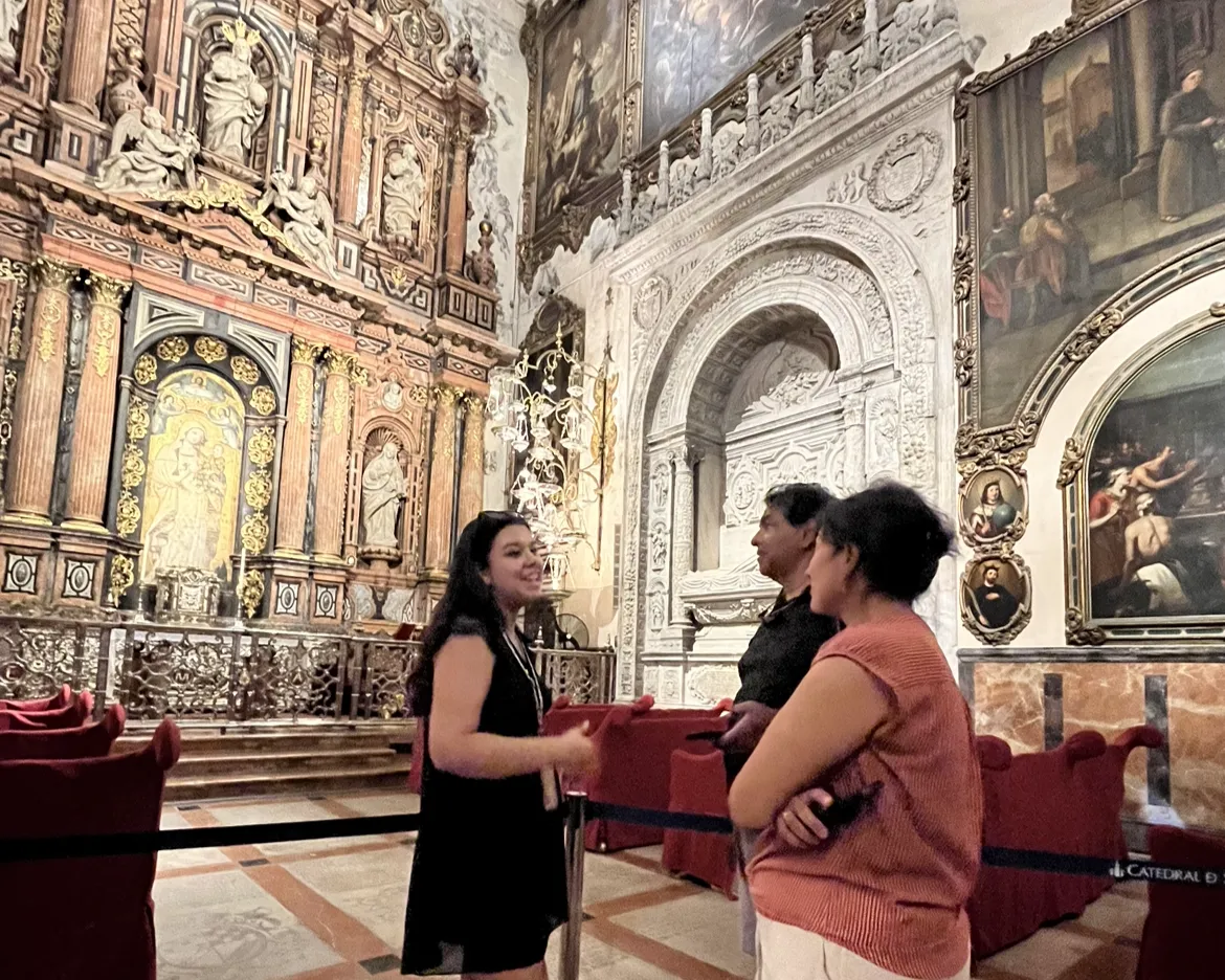 A guide talks with visitors inside Seville Cathedral beside its gilded altarpieces