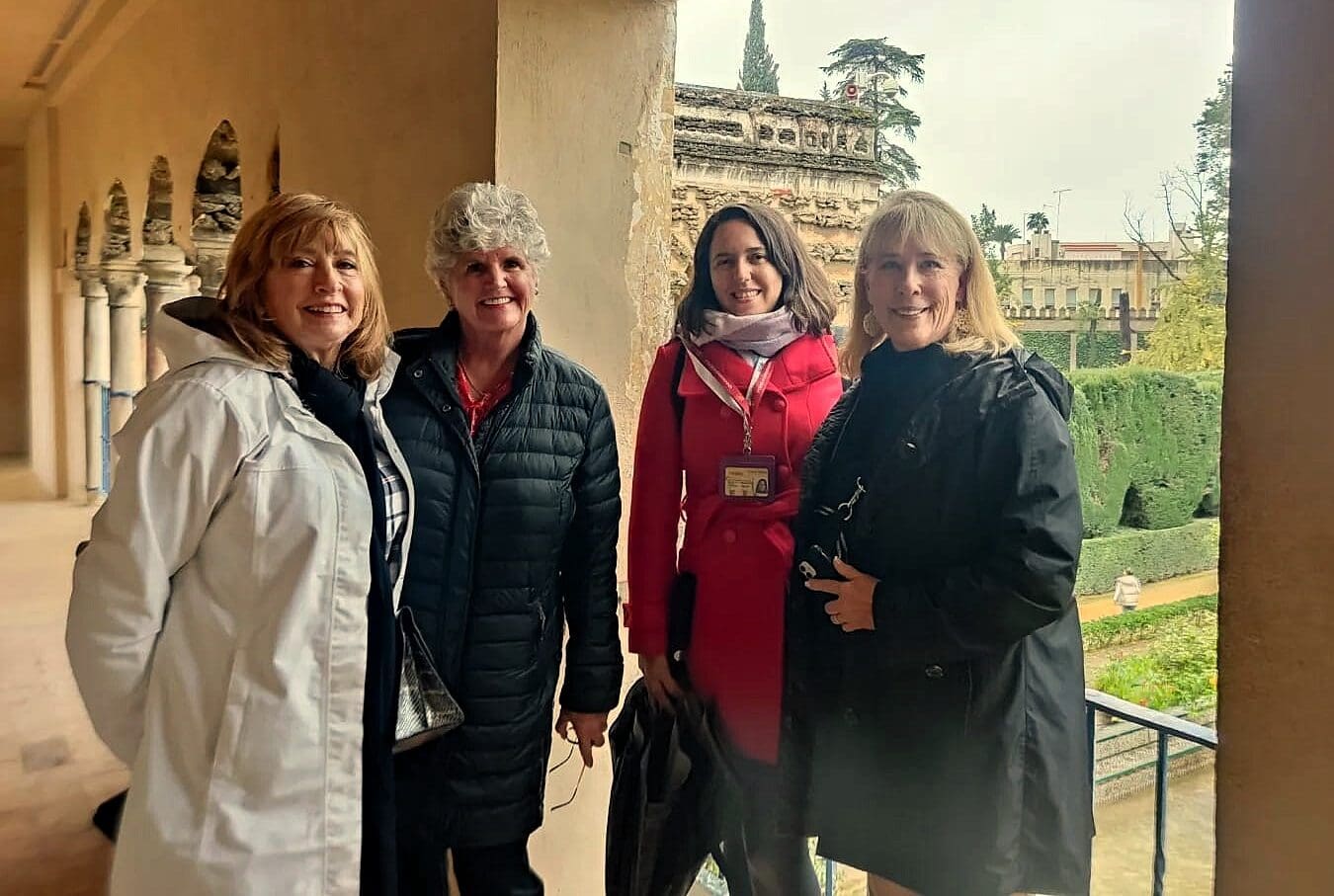Visitors in winter coats smile in a gallery above the Royal Alcázar gardens on a mild Seville winter day