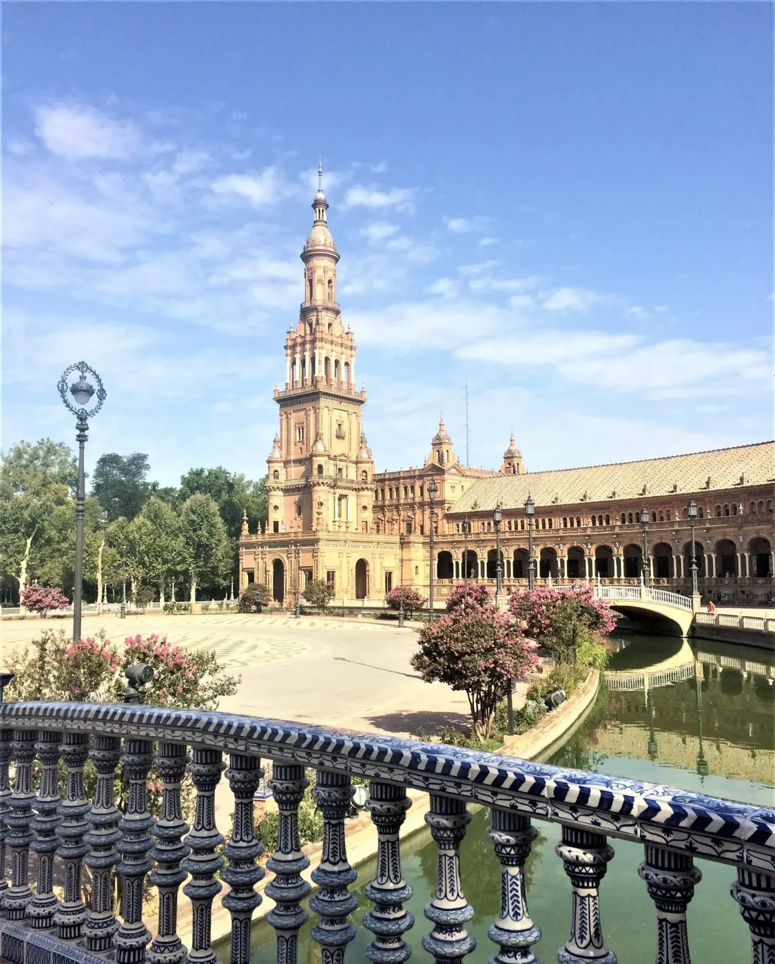 Ceramic-tiled balustrade and canal framing a tower of Plaza de España, an iconic Seville tourism experience